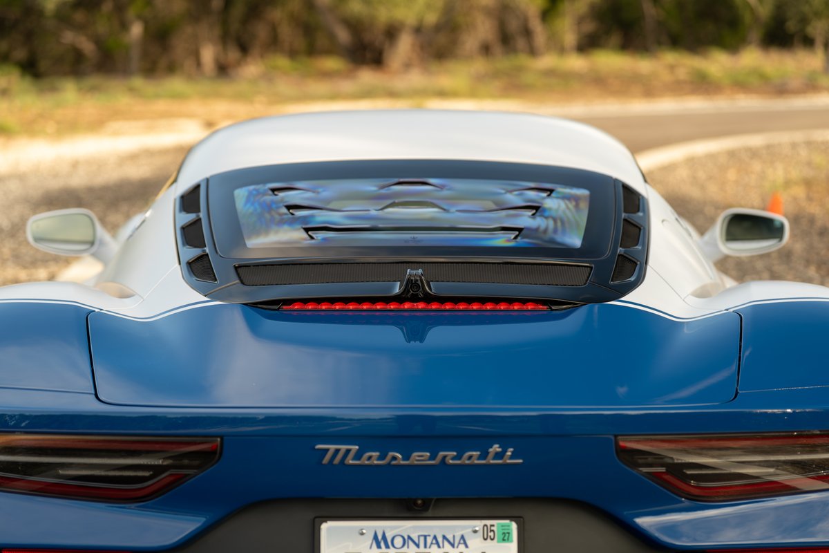 Rear view of a 2024 Maserati MC20 Icona in blue with white racing stripes and a black vented engine cover.