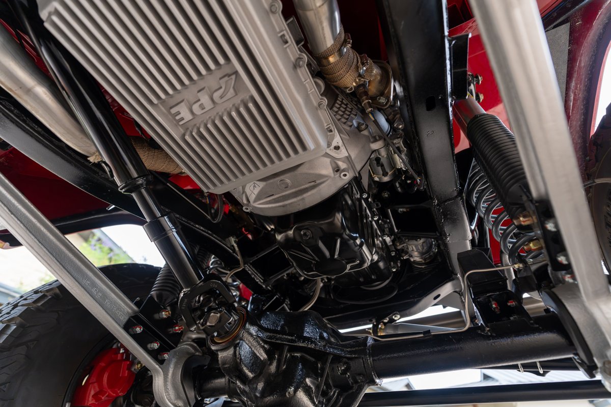 Underbody of a red 1966 Ford Bronco, showing a PPE aluminum transmission pan and suspension.