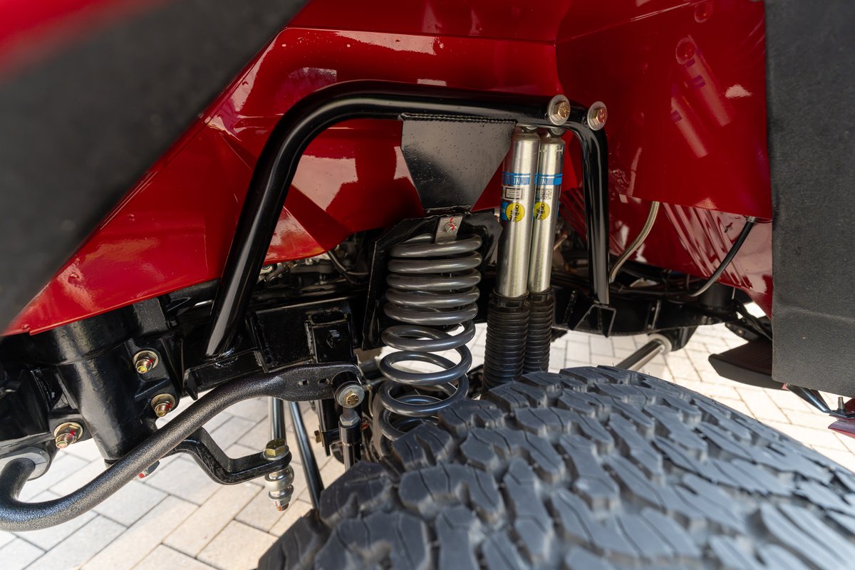Red 1966 Ford Bronco rear suspension with Bilstein shocks, coil springs, and off-road tire.