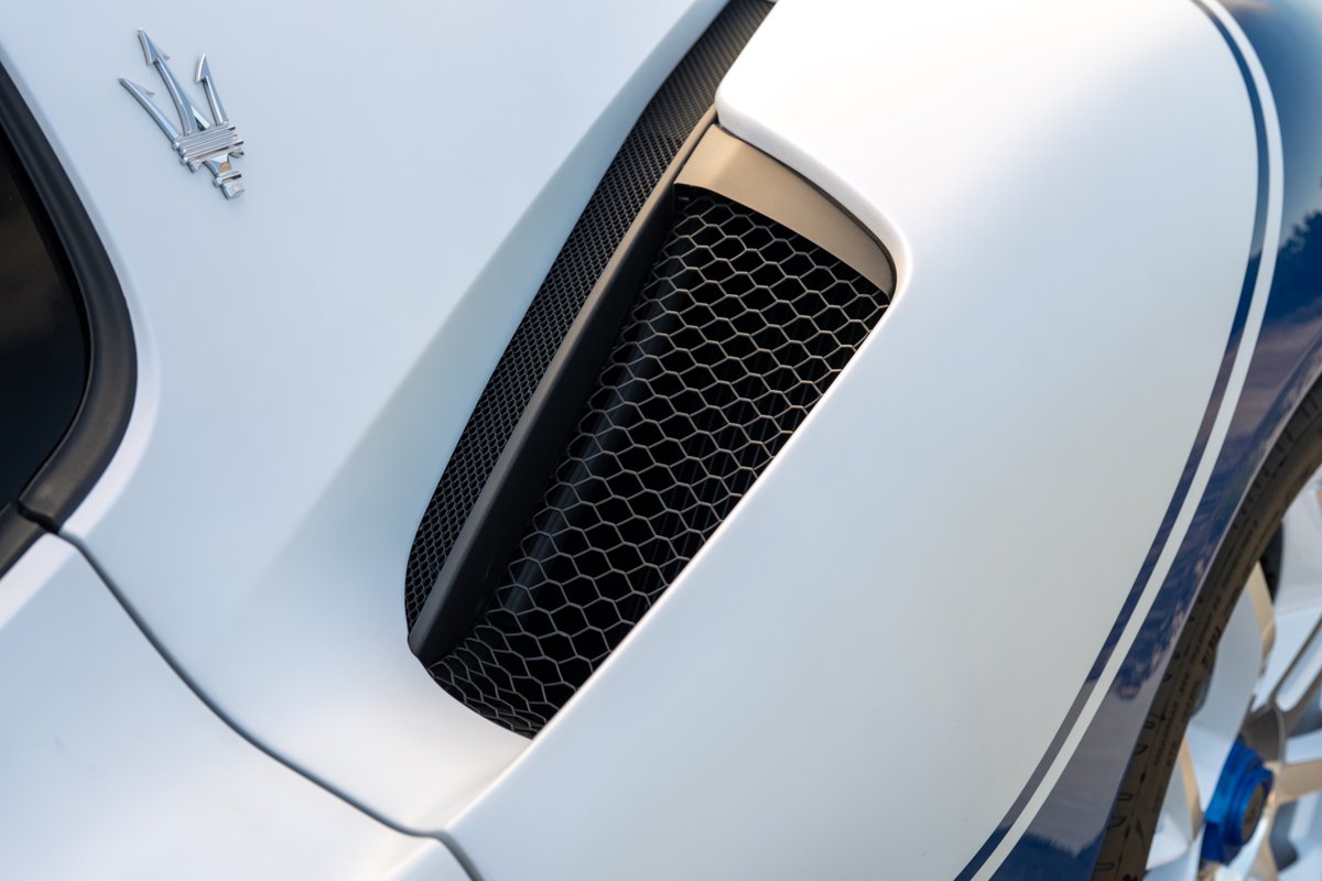 Maserati MC20 Icona: white body with blue racing stripes, hexagonal grille vent, trident emblem.
