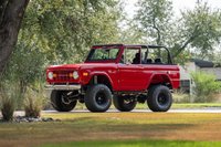 Red 1966 Ford Bronco with black rims, off-road tires, and a roll cage.