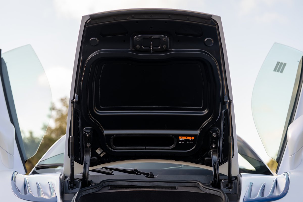 Close-up of the open front trunk (frunk) of a white 2024 Maserati MC20 Icona, showing hinges and interior trim.
