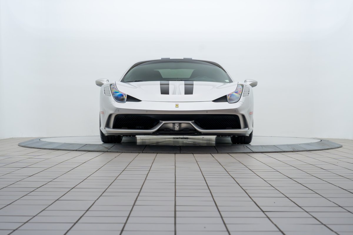 Front view of a silver 2015 Ferrari 458 Speciale with black racing stripes.