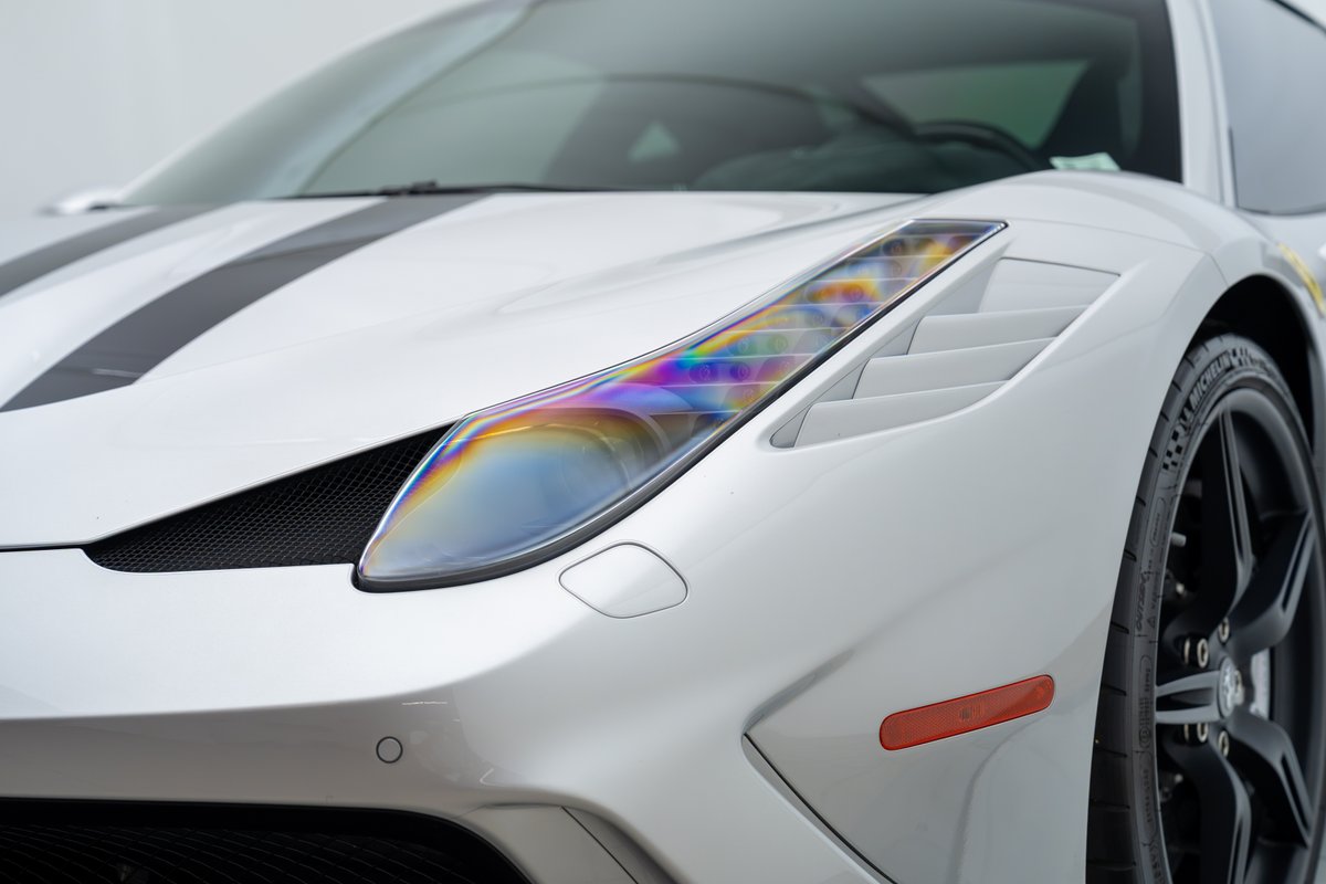 2015 Ferrari 458 Speciale in white with black racing stripes, rainbow headlight detail, and black rims.