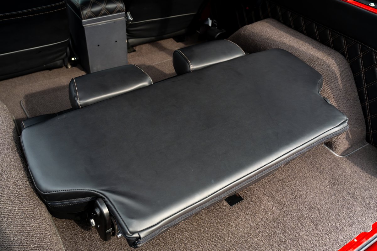 1966 Ford Bronco rear jump seat folded out, black upholstery with white stitching, diamond-pattern trim.