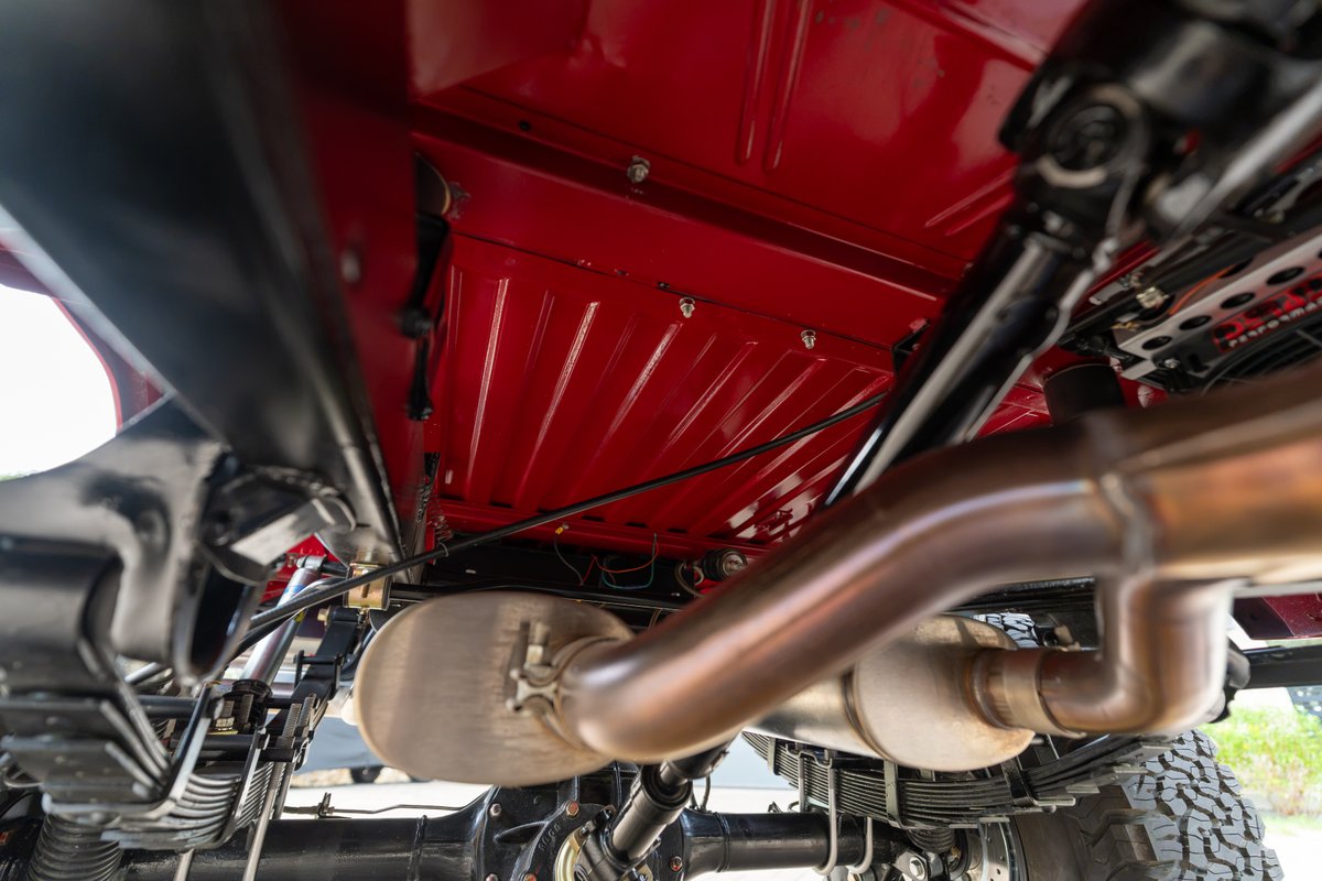 Underside of a red 1966 Ford Bronco, showing suspension, exhaust and drivetrain.