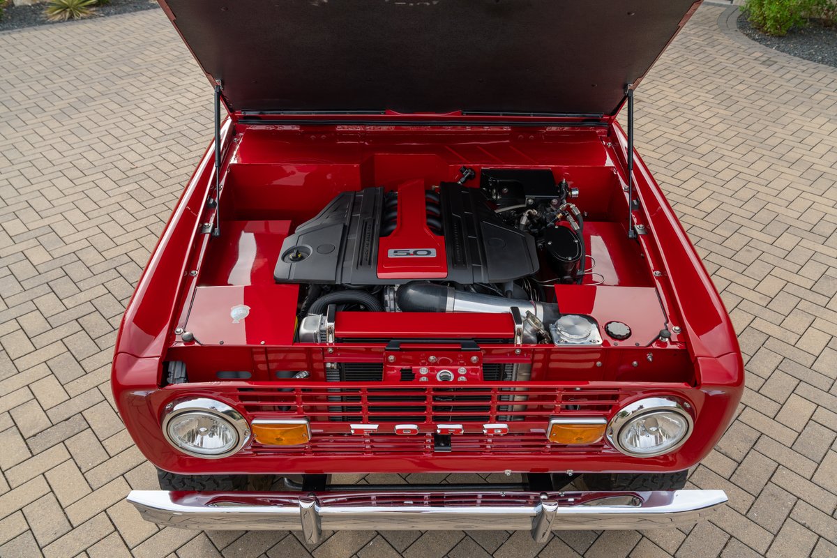 Custom red 1966 Ford Bronco with a Ford 5.0 Coyote V8 engine and chrome trim.