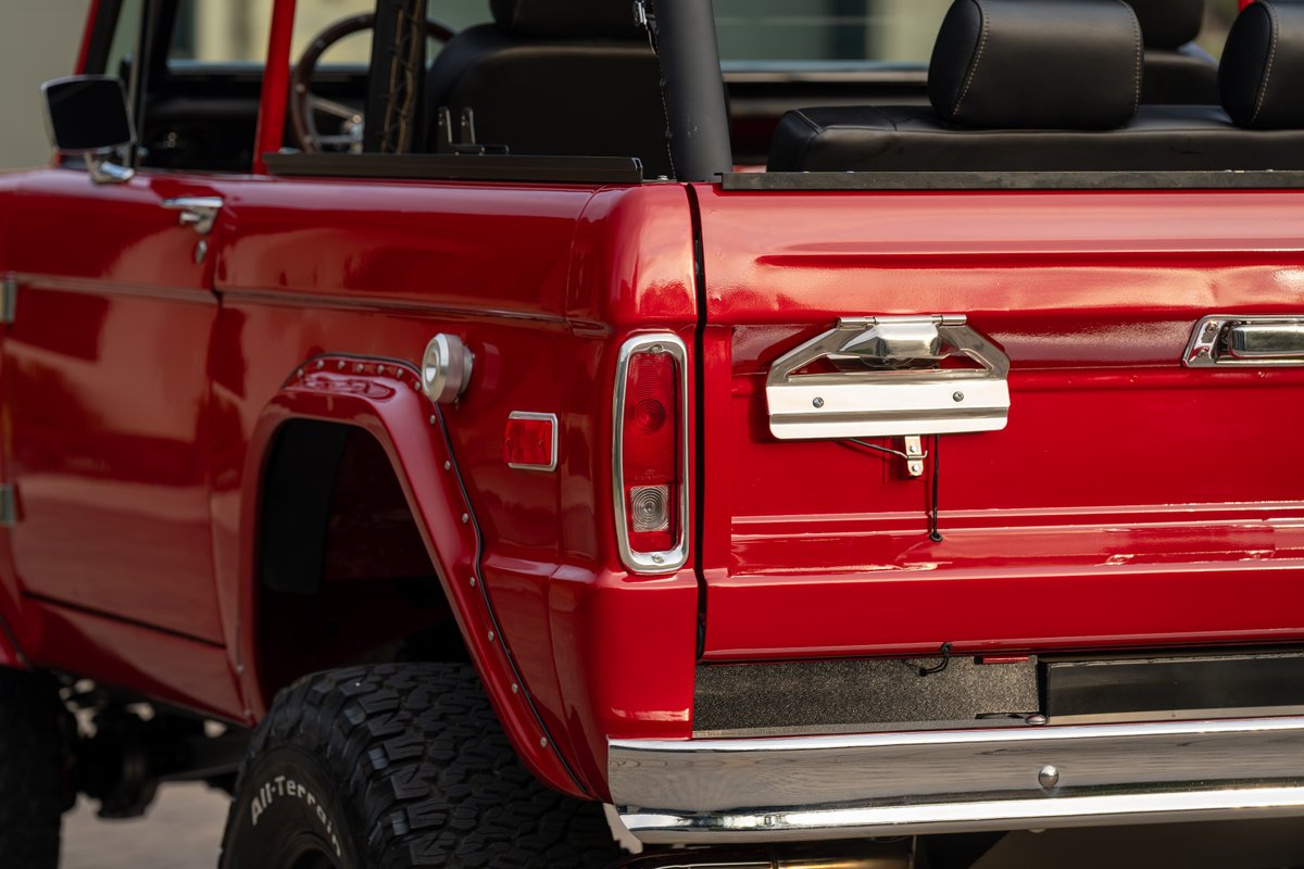 Red 1966 Ford Bronco rear quarter panel, tailgate handle, and chrome bumper.