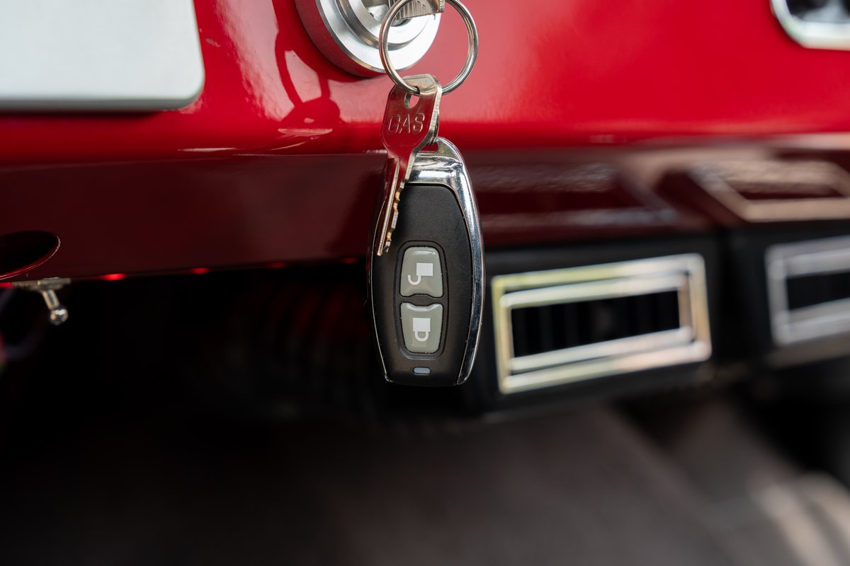 1966 Ford Bronco's key fob hangs from ignition. Red dash, chrome trim, air vents.