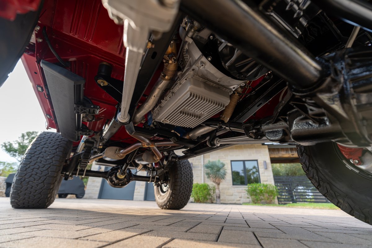 Underside of a red 1966 Ford Bronco showing transmission, exhaust, suspension, and tires.