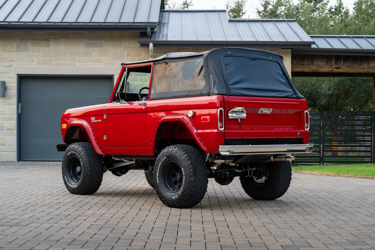 Red 1966 Ford Bronco by Atlas Broncos, with black soft top and aggressive off-road tires on black rims.