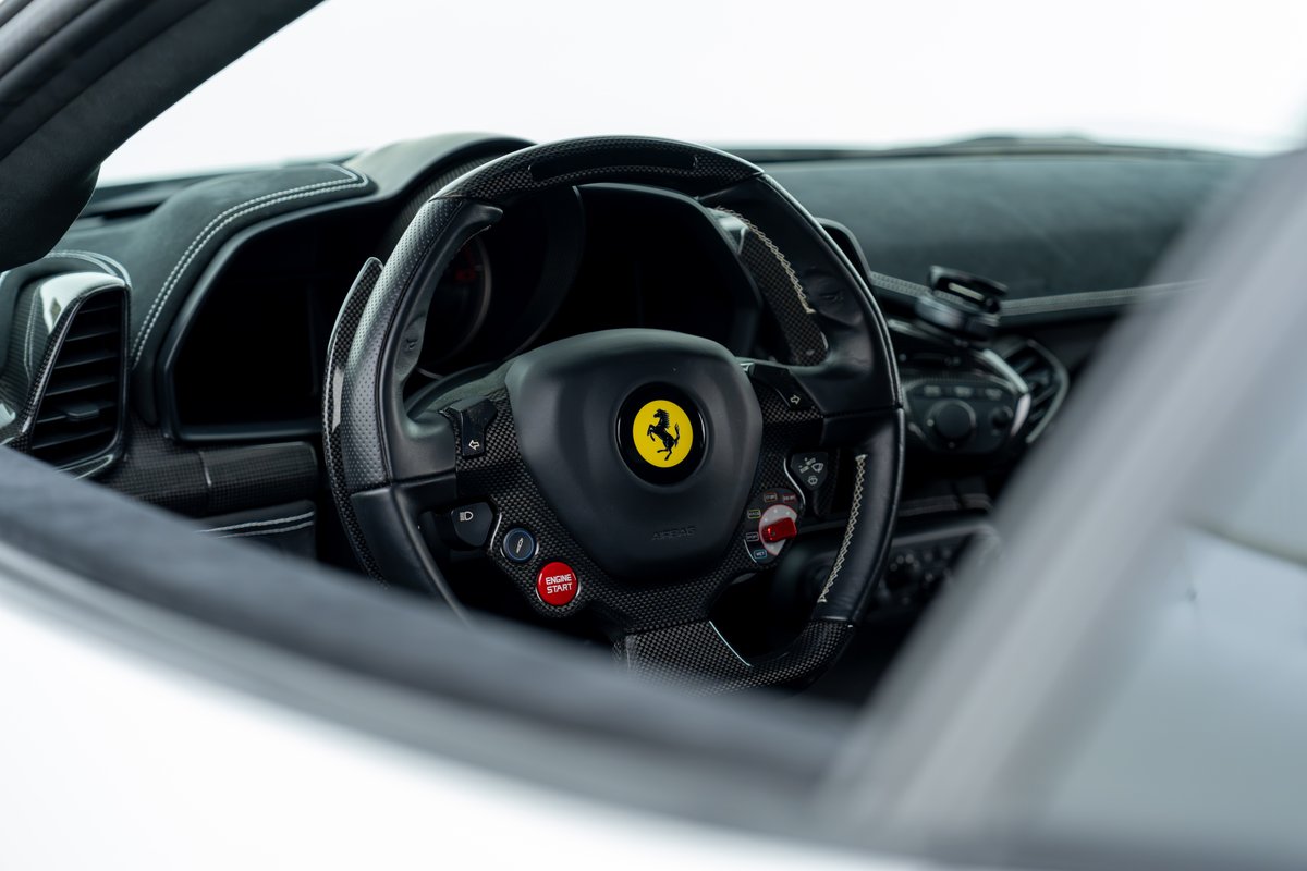 Interior view of a 2015 Ferrari 458 Speciale with carbon fiber trim and a red engine start button.