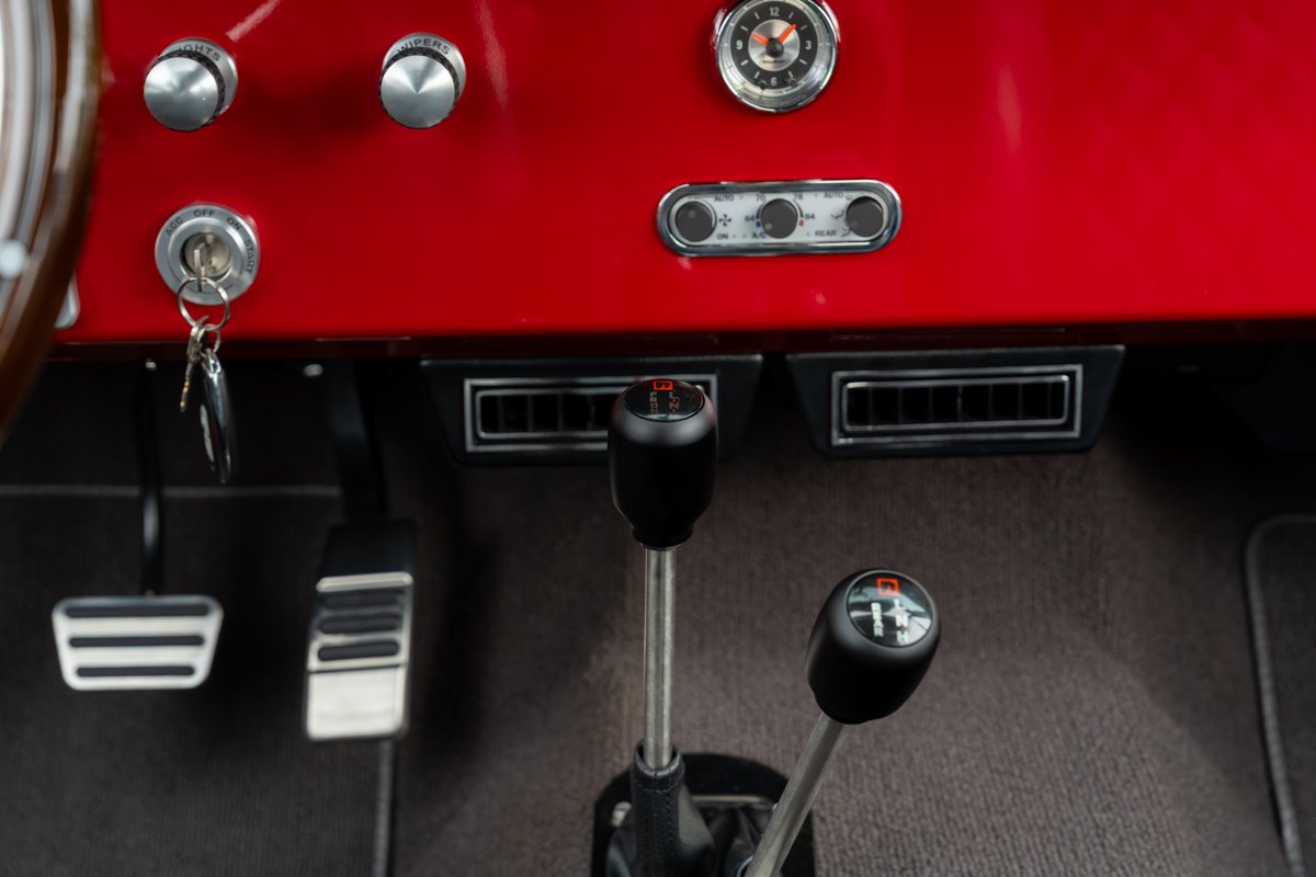 1966 Ford Bronco by Atlas Broncos: Black shifter knobs on manual transmission, metal floor pedals, and red dashboard with chrome accents.