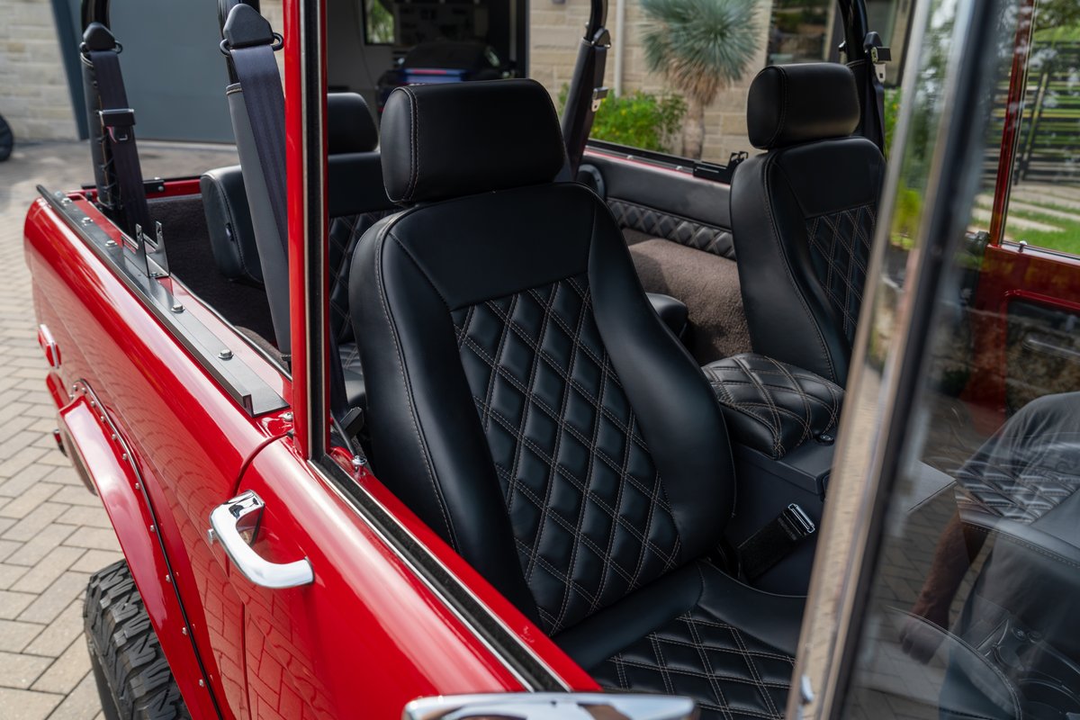 1966 Ford Bronco interior with diamond-stitched black leather seats and red exterior trim.