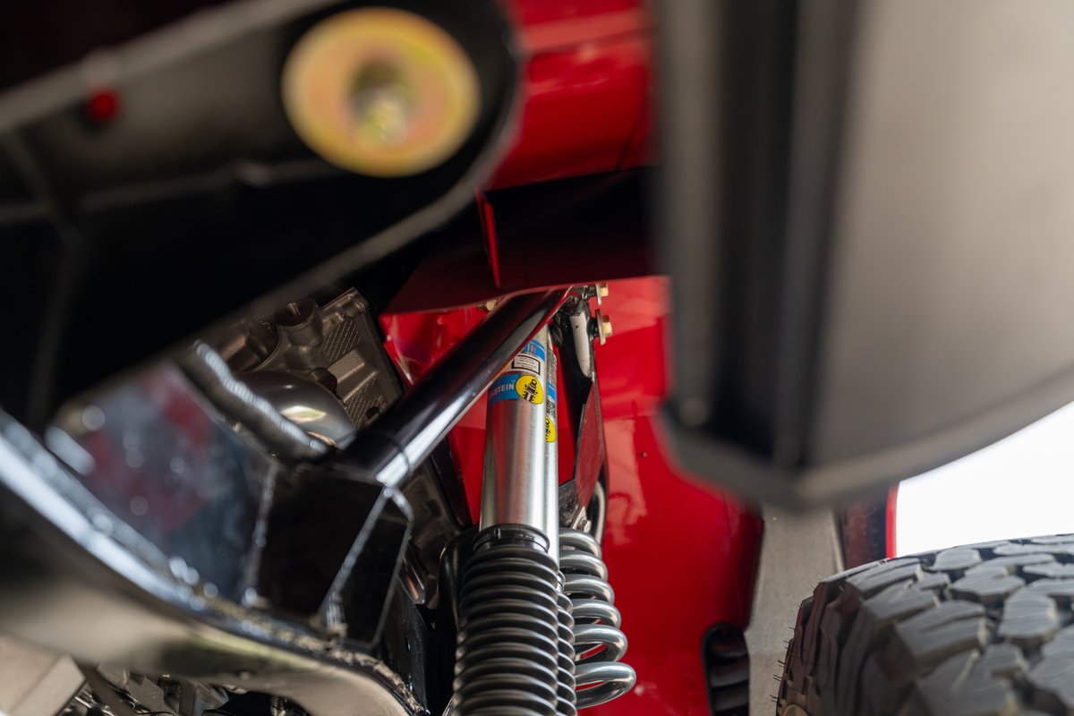 Close-up of a red 1966 Ford Bronco's suspension with Bilstein shocks and coil springs.