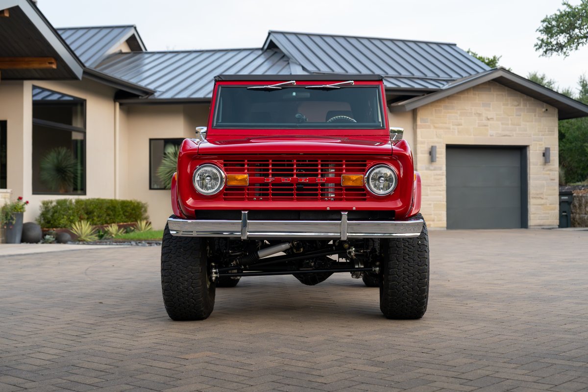 1966 red Ford Bronco, front view, with large off-road tires and chrome trim.
