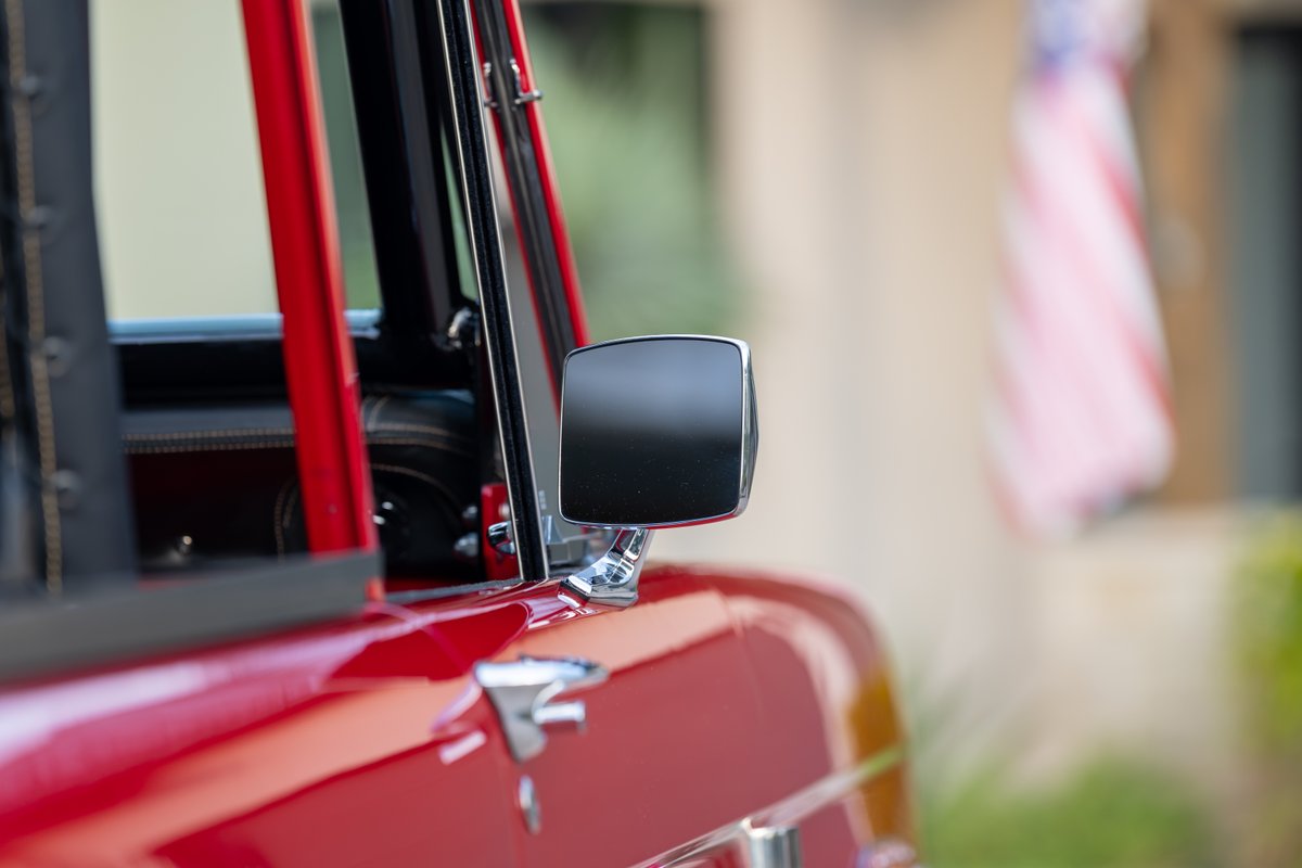 1966 Ford Bronco: Closeup of red exterior with chrome trim and side mirror.