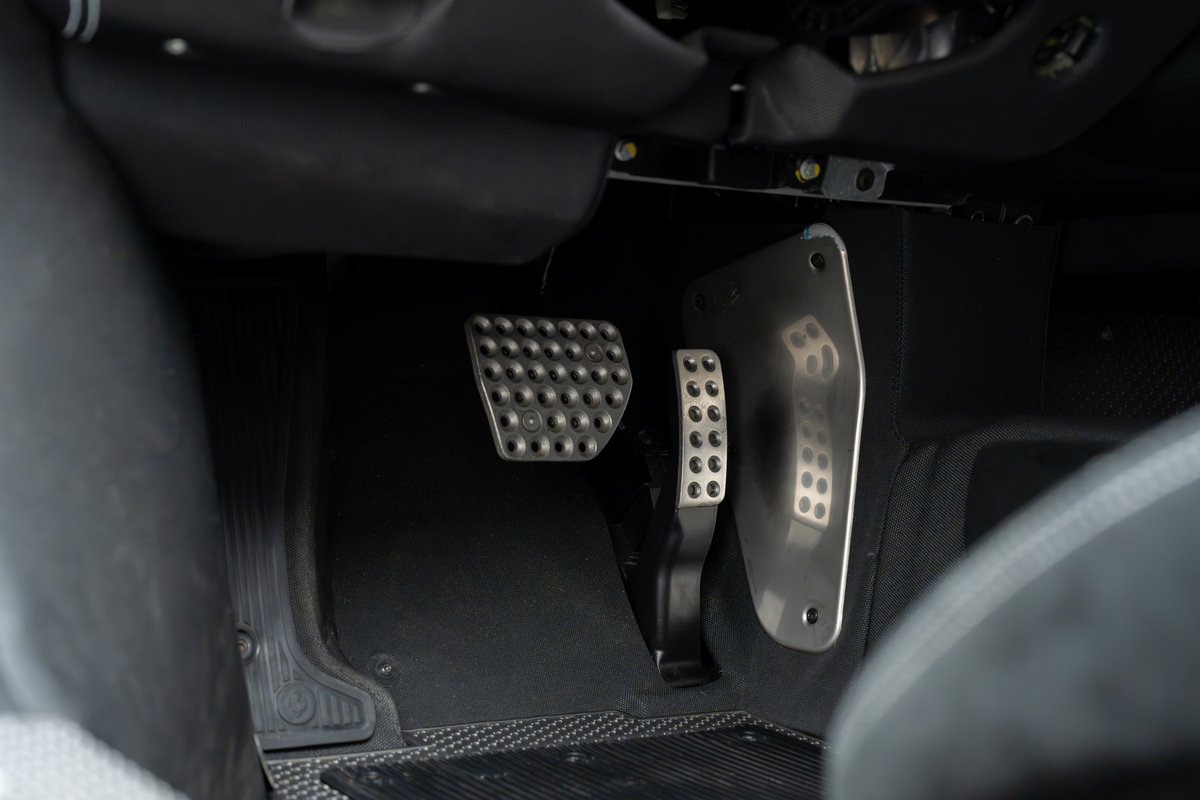 Close-up of the driver's footwell in a 2015 Ferrari 458 Speciale, showing perforated aluminum clutch, brake, and throttle pedals.