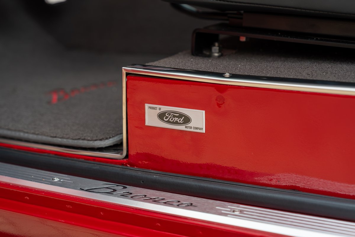 Red 1966 Ford Bronco has "Bronco" door sill trim and a "Product of Ford Motor Company" badge.