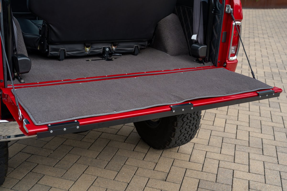 1966 red Ford Bronco tailgate with charcoal carpet mat and black trim.