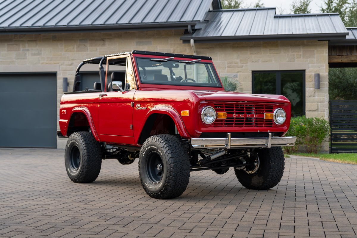 Red 1966 Ford Bronco with black roll cage, chrome bumper, and off-road rims.