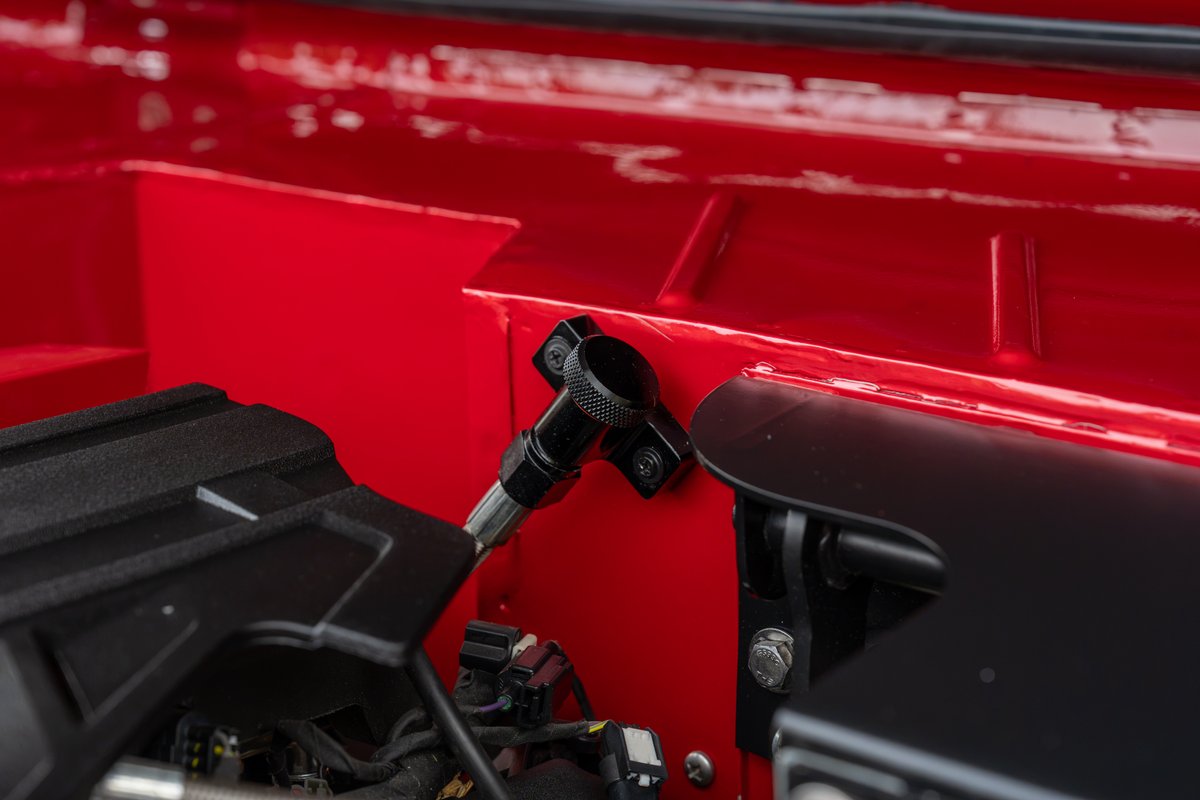 Black anodized AN fitting with knurled knob mounted on red 1966 Ford Bronco firewall.