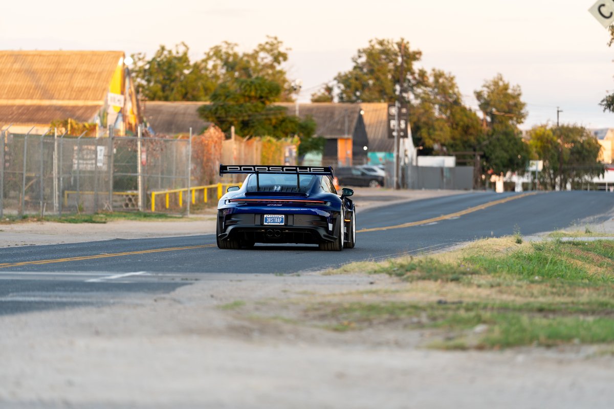 Rear view of a dark blue 2025 Porsche 911 GT3 RS with a large rear wing and gold-accented rims.