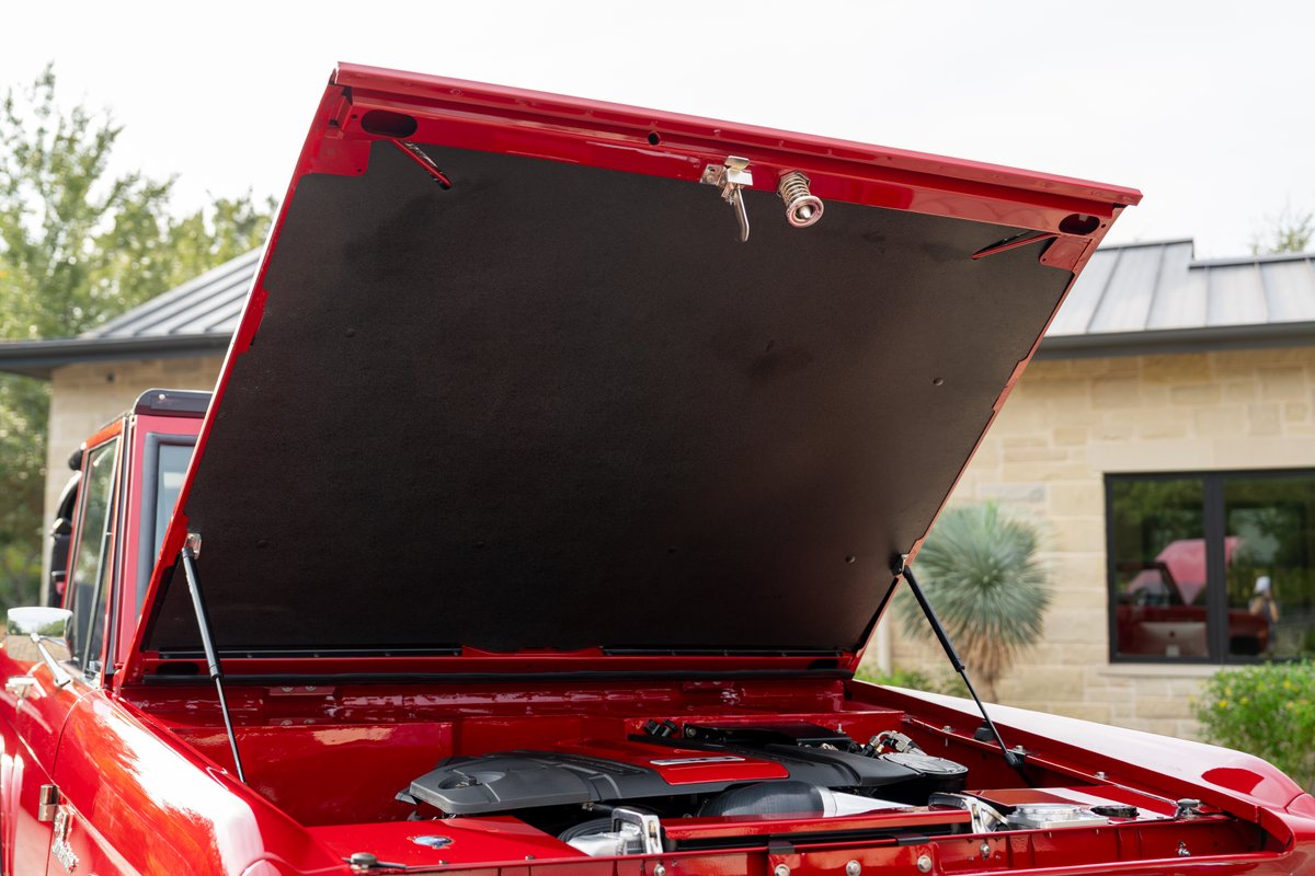 Red 1966 Ford Bronco by Atlas Broncos shows exposed engine bay with black underside of hood.