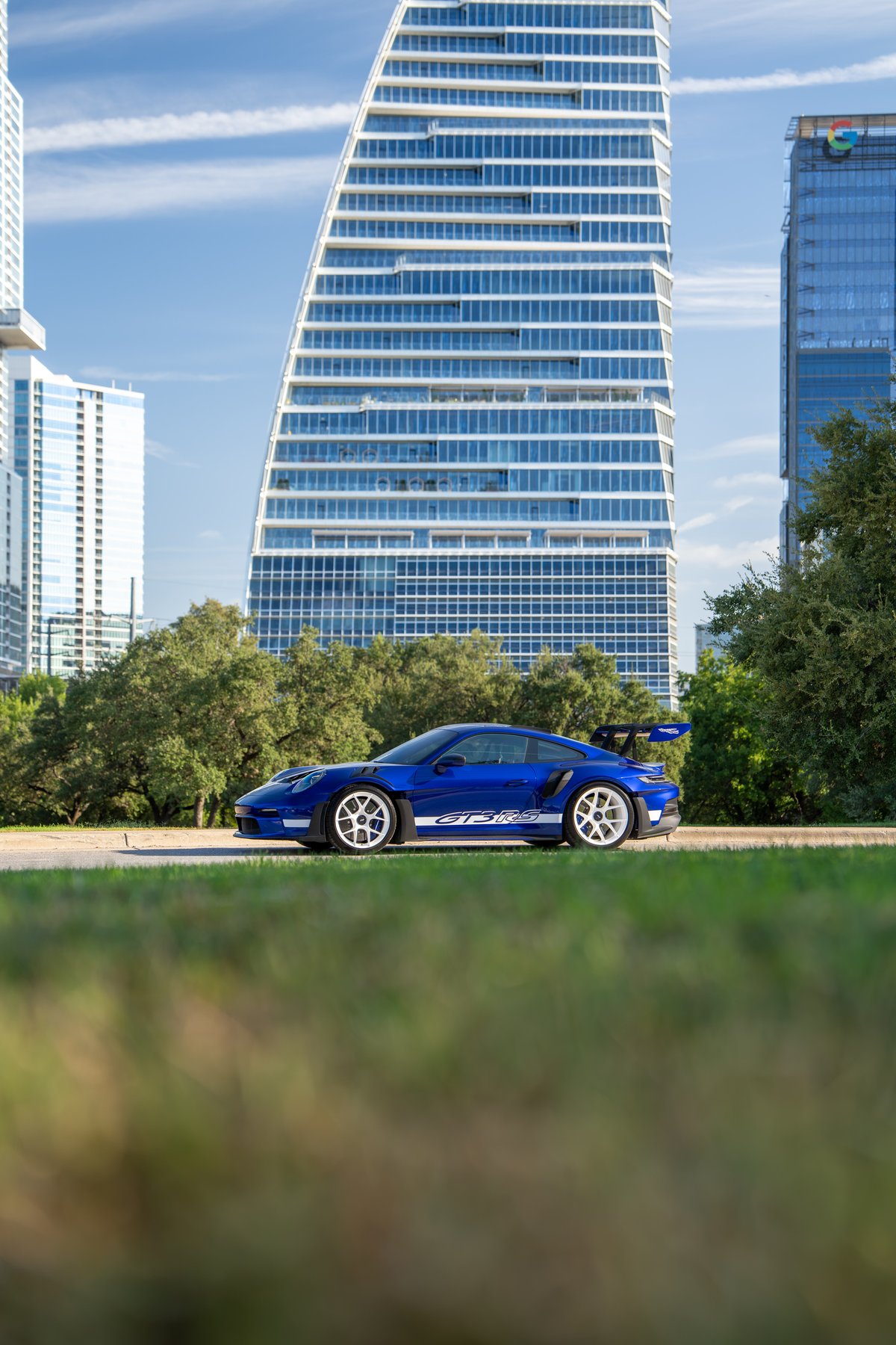 Blue 2025 Porsche 911 GT3 RS with white rims and GT3 RS livery parked in front of buildings.