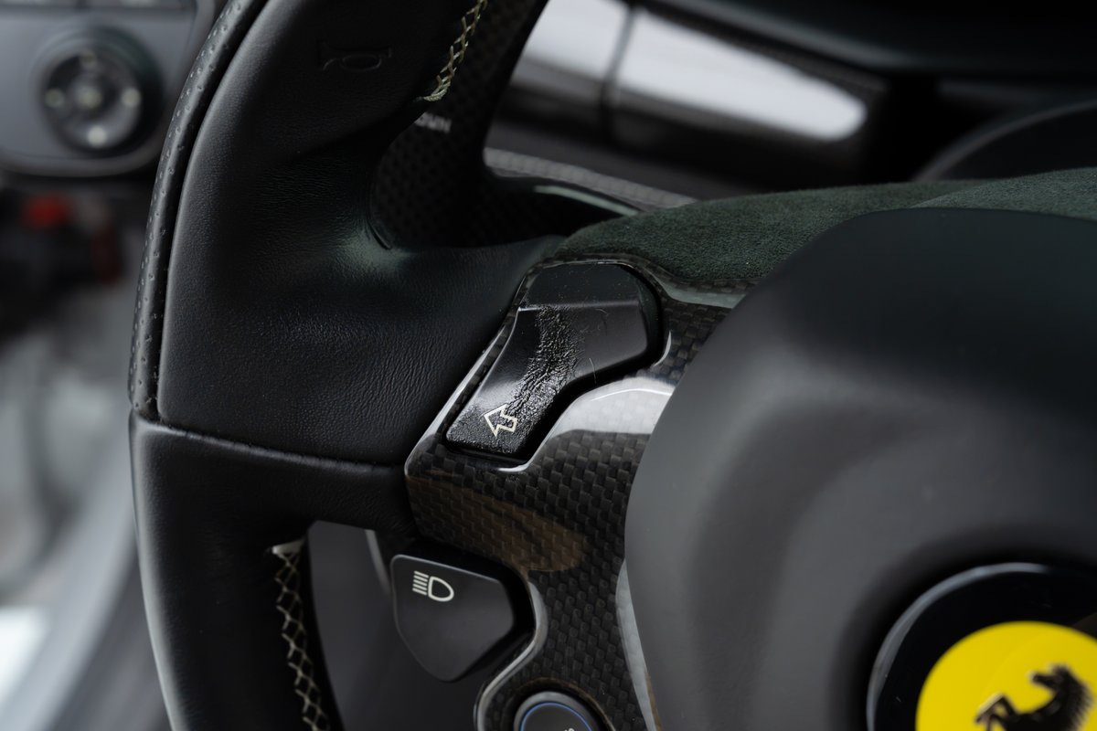 Steering wheel detail on a 2015 Ferrari 458 Speciale, showing carbon fiber trim and a button with an arrow icon.