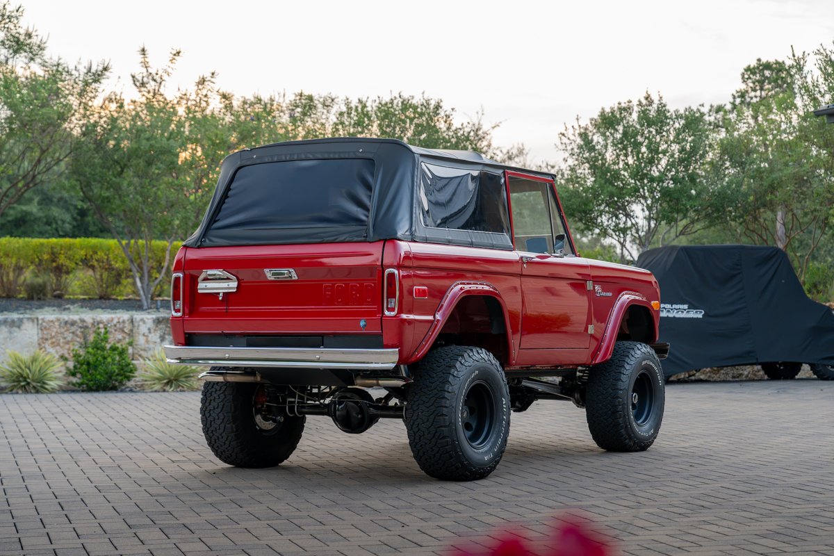 Red 1966 Ford Bronco with black soft top, chrome bumper, and black rims.