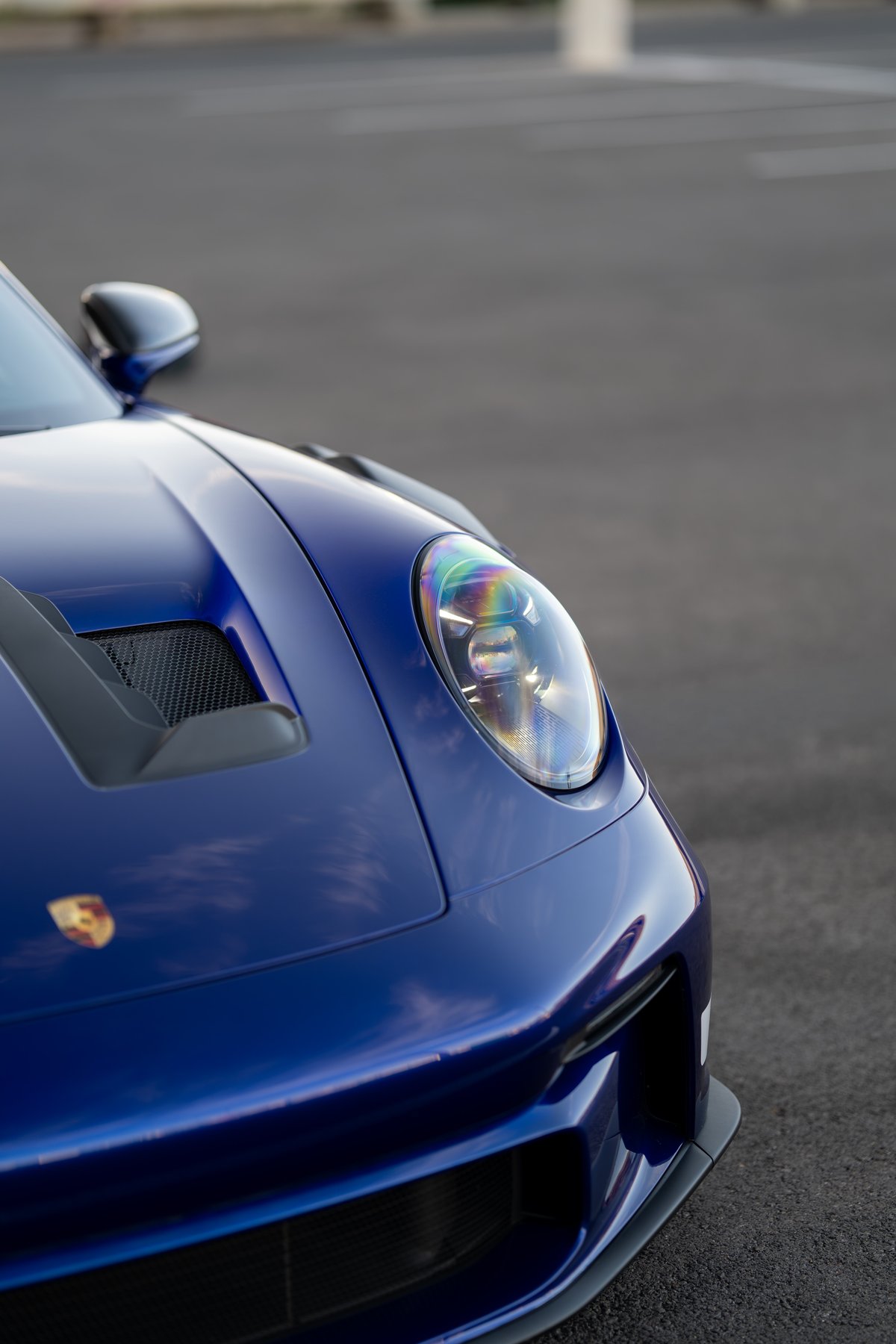 Blue 2025 Porsche 911 GT3 RS front fender with hood vent, emblem, and Xenon headlight.