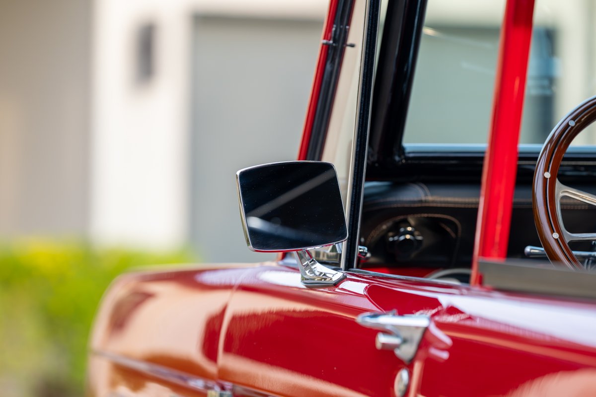 Red 1966 Ford Bronco with polished chrome side mirror and a wooden steering wheel.
