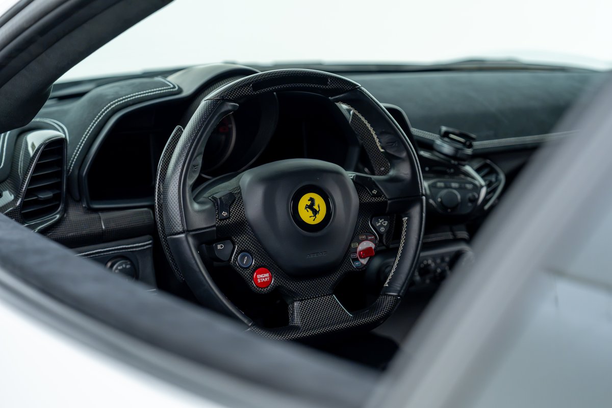 2015 Ferrari 458 Speciale interior: carbon fiber steering wheel, red engine start button, yellow Ferrari badge.