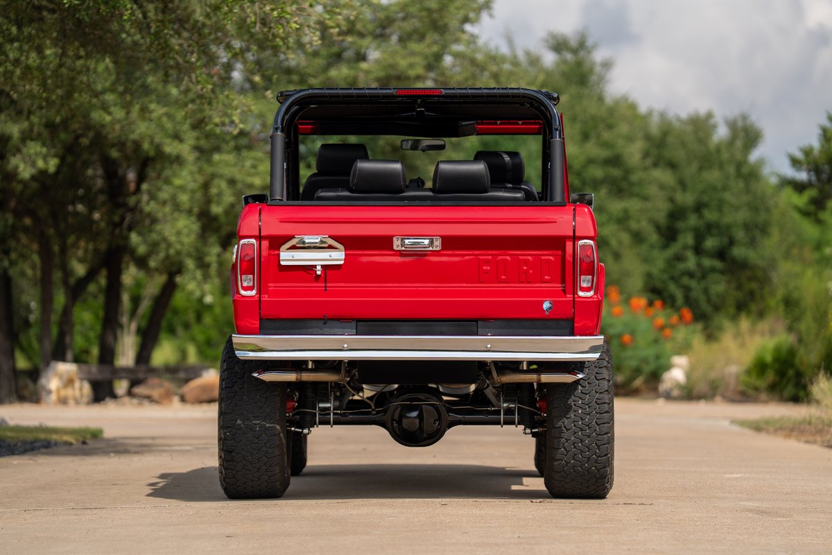 1966 Ford Bronco in red, with chrome trim and large off-road tires.