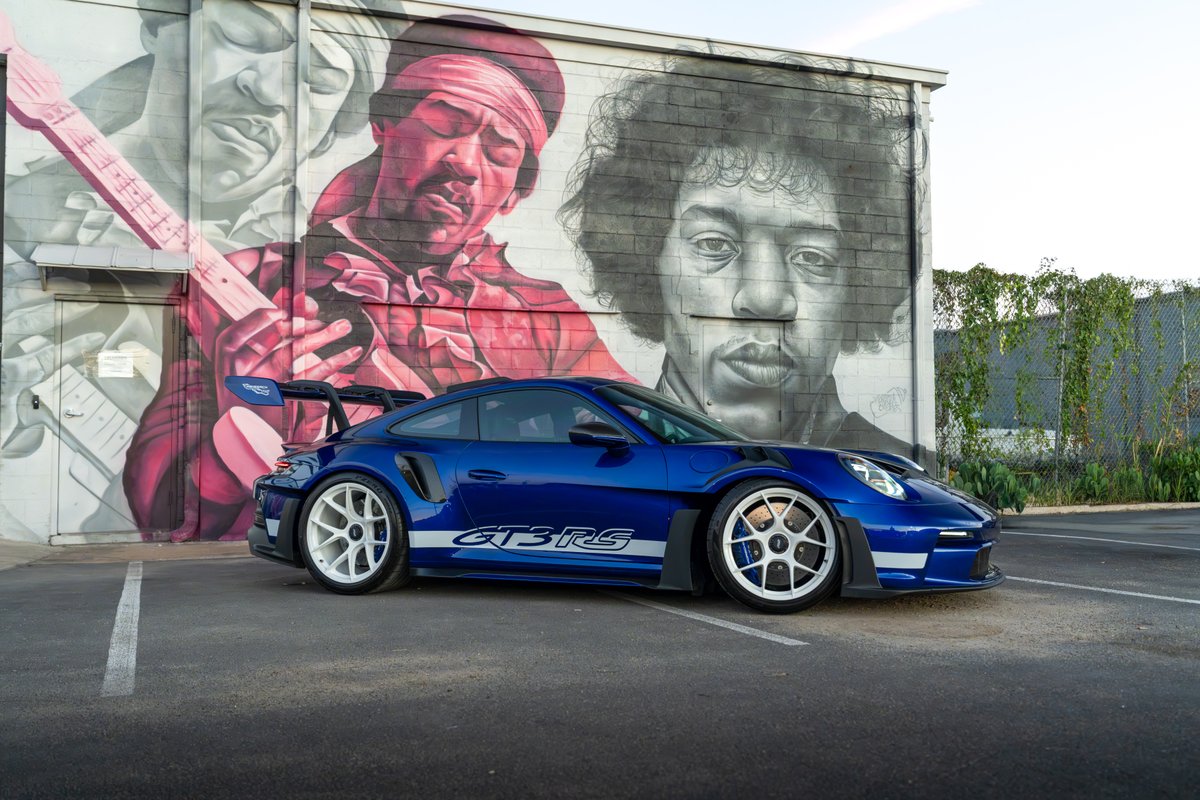 A blue 2025 Porsche 911 GT3 RS with white rims, GT3 RS livery, and a large rear wing.