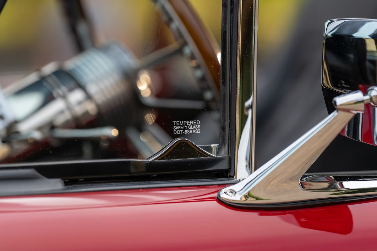 Close up of a red 1966 Ford Bronco, showing tempered safety glass and chrome mirror.