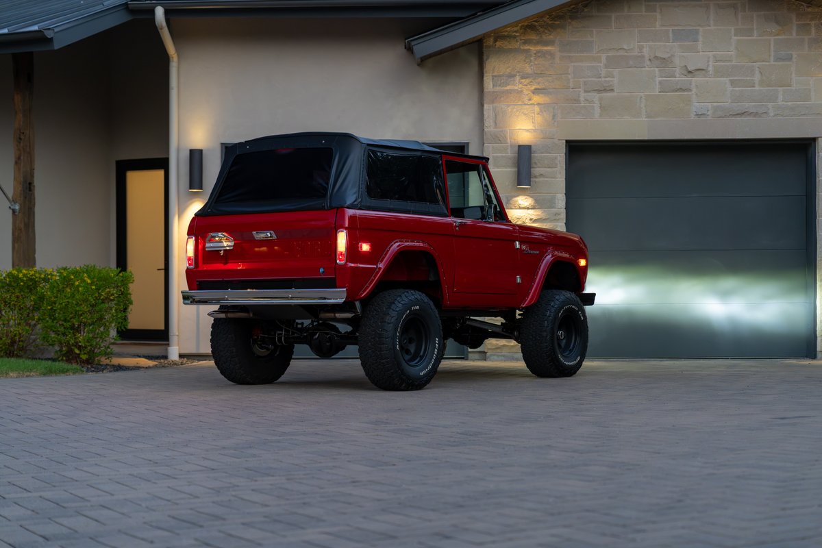 Red 1966 Ford Bronco with black soft top and rugged off-road tires.
