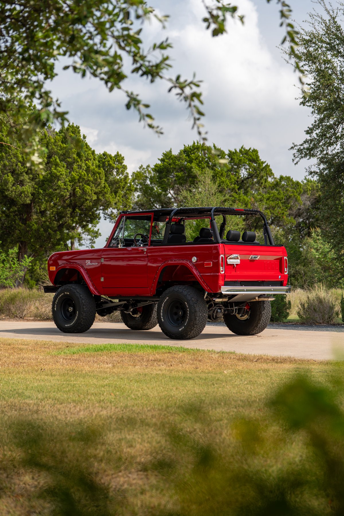 Rear 3/4 view of a red 1966 Ford Bronco by Atlas Broncos with black rims and off-road tires.
