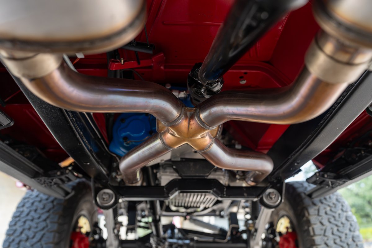 1966 Ford Bronco undercarriage with custom dual exhaust system. Red paint, black trim.