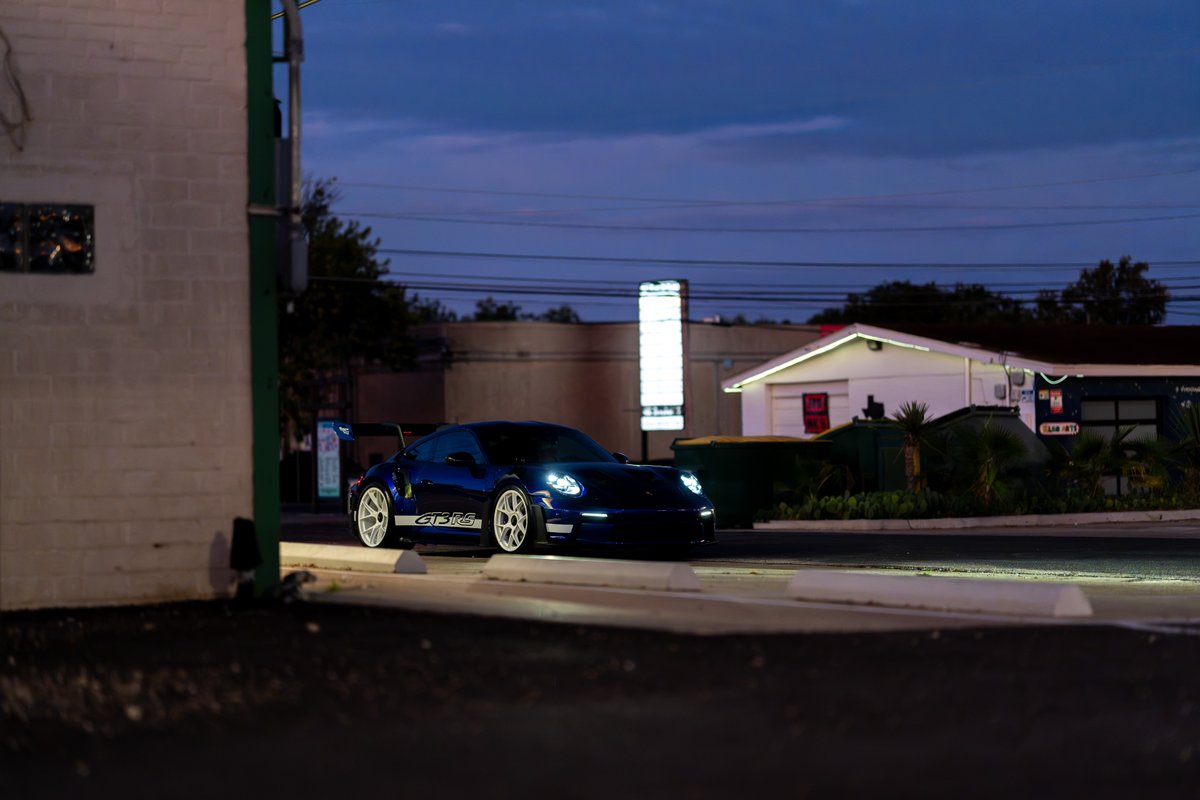 A dark blue 2025 Porsche 911 GT3 RS with white rims and GT3 RS livery sits at dusk.