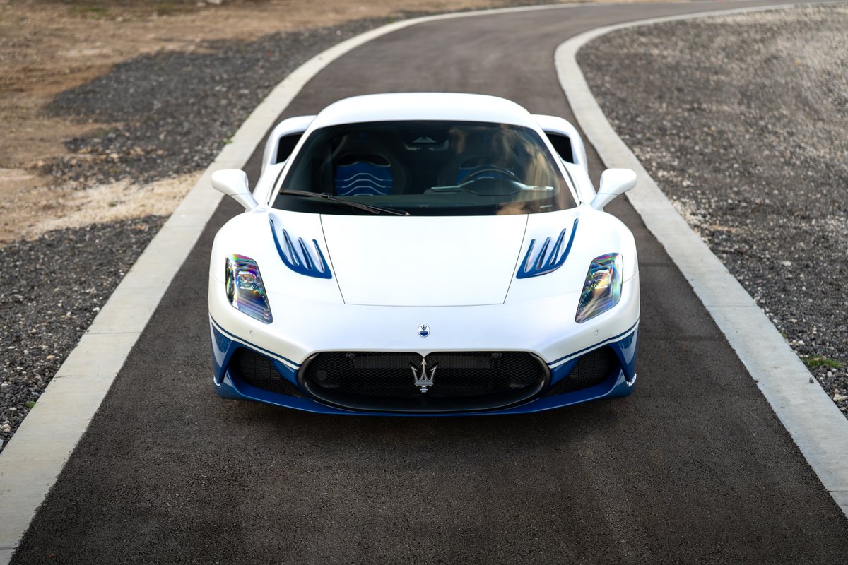 Front view of a white 2024 Maserati MC20 Icona with blue livery accents and racing stripes on the hood.