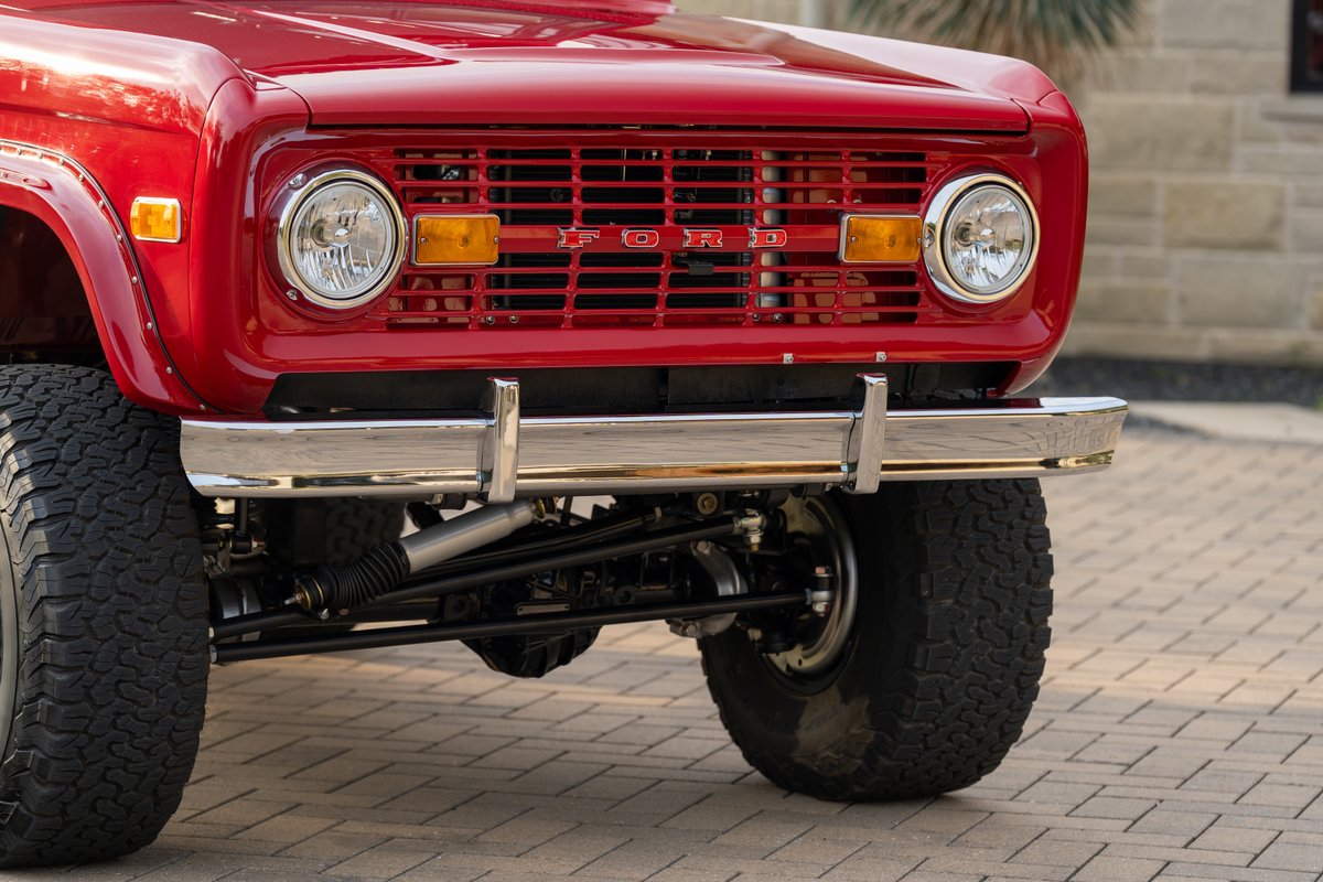 1966 red Ford Bronco front grille, chrome bumper, and large tires.