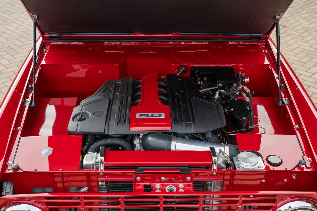 Red 1966 Ford Bronco with a Ford 5.0L Coyote V8 engine, custom intake, and polished components.