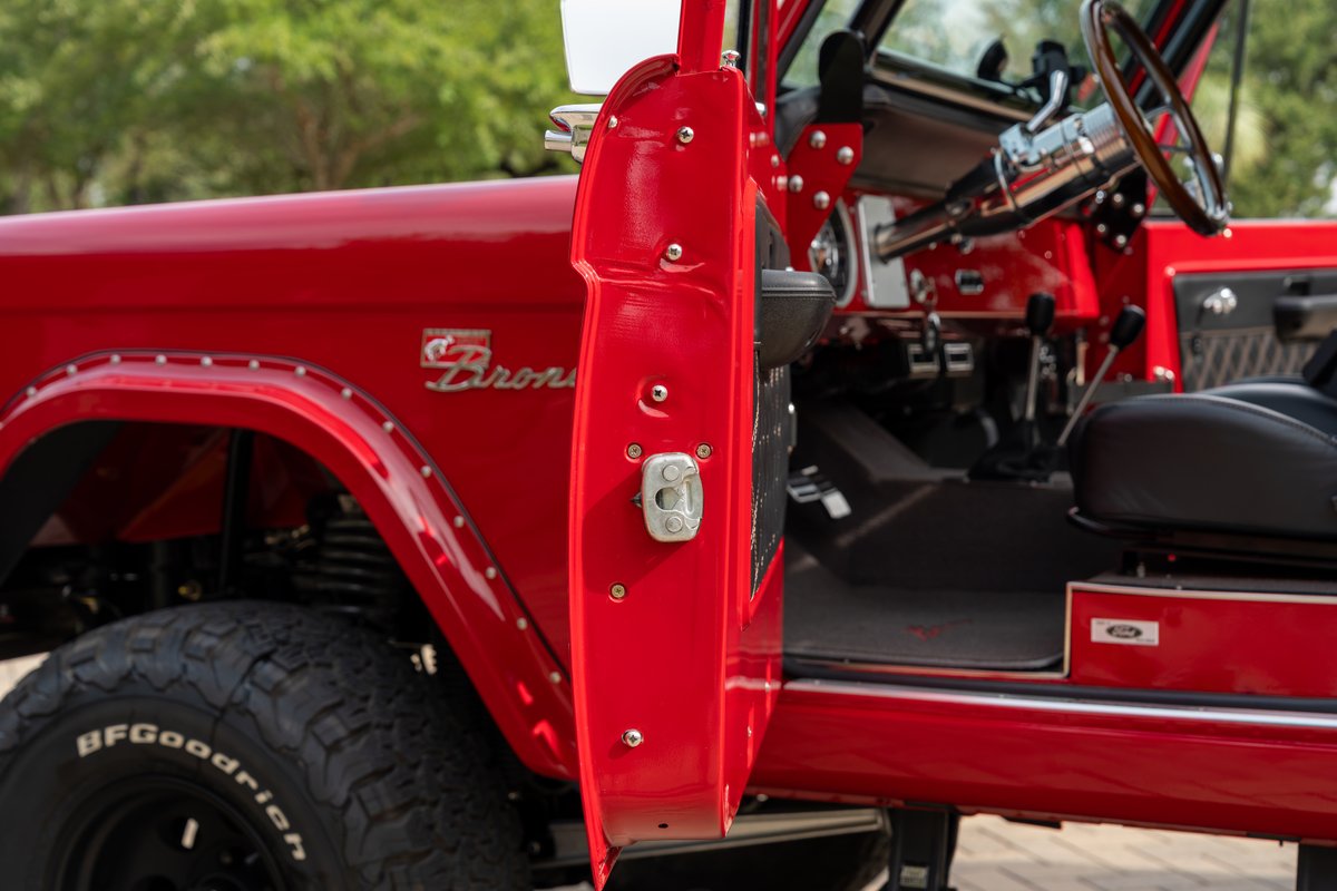 Red 1966 Ford Bronco with chrome trim, studded fender flares, and black BFGoodrich tires.