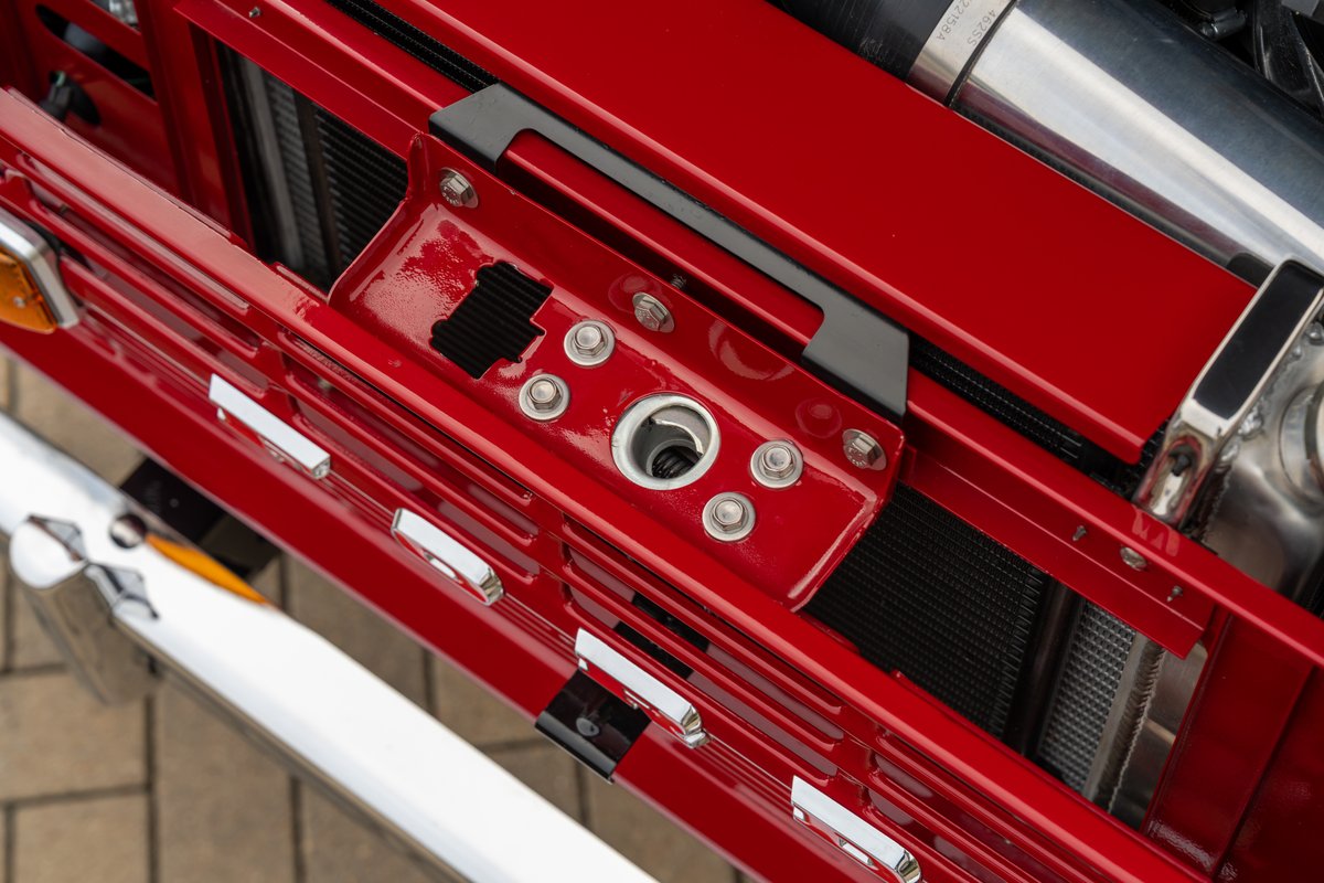 Close-up of a red 1966 Ford Bronco's grille, showing chrome trim and a black latch.