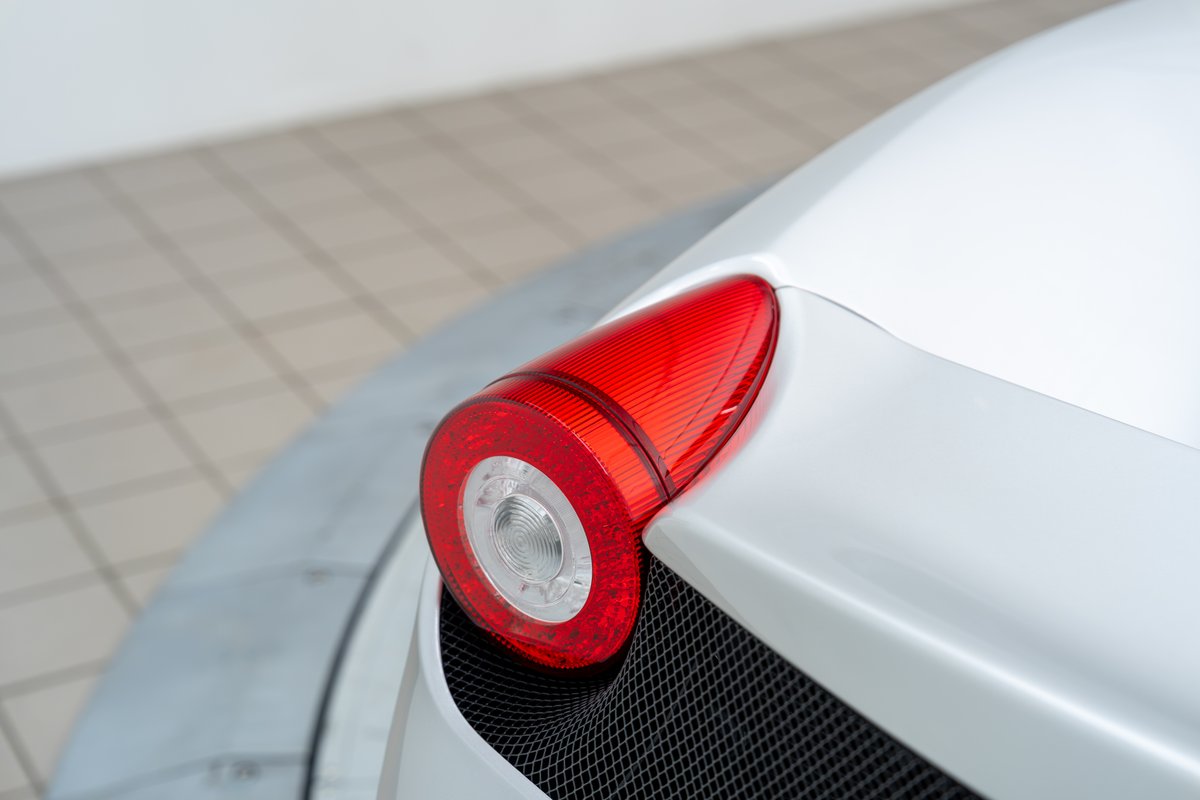 Close-up of a white 2015 Ferrari 458 Speciale's red LED tail light and black mesh grille.