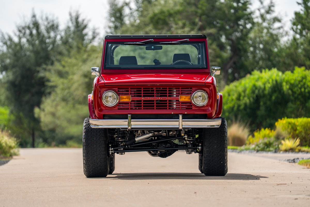 Front view of a red 1966 Ford Bronco by Atlas Broncos with large off-road tires and chrome bumper.