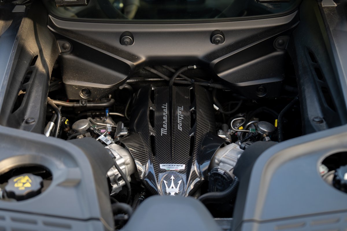 Close-up of a Maserati MC20 Icona engine bay, featuring carbon fiber engine covers and the trident emblem.