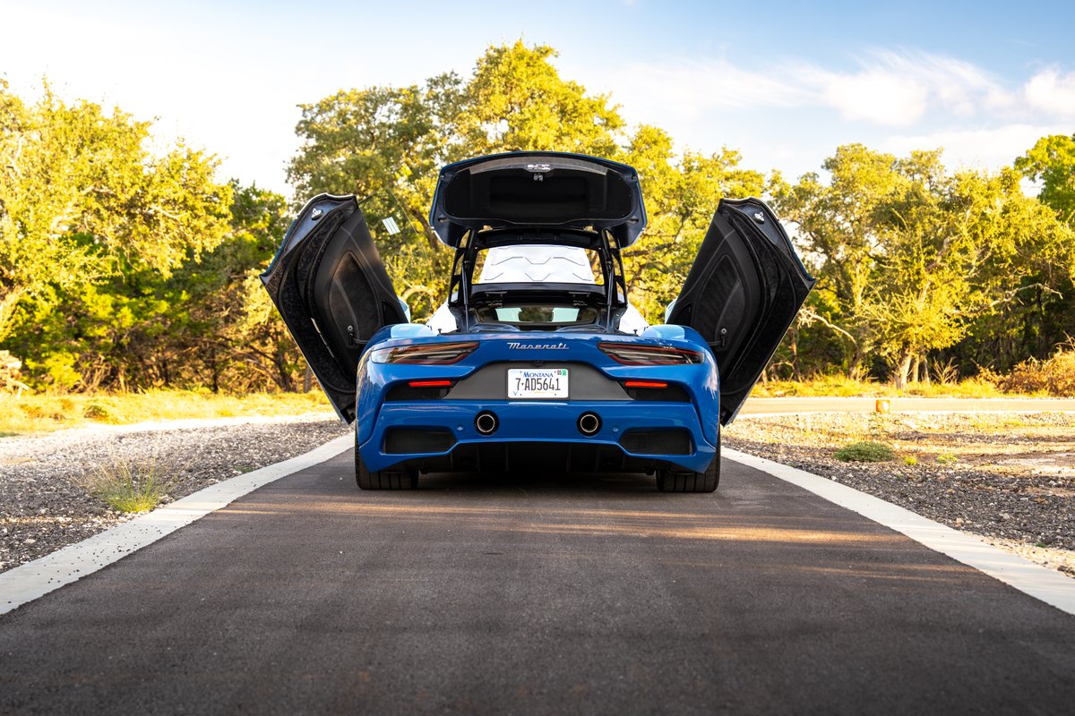 Rear view of a blue 2024 Maserati MC20 Icona with dihedral doors and trunk open.